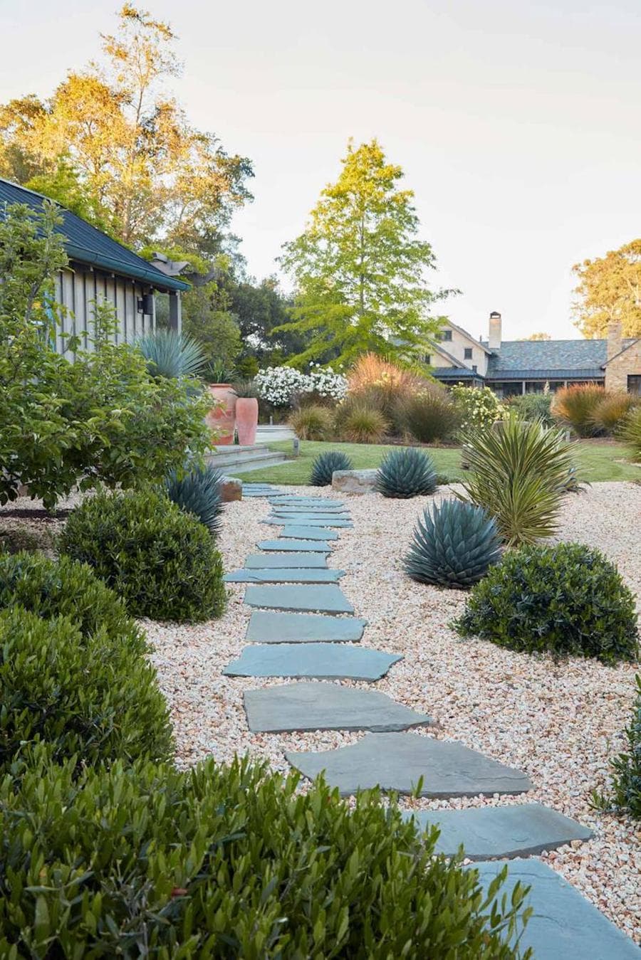 Jardín seco con arbustos, piedras y un gran camino hecho de grandes pastelones verdes