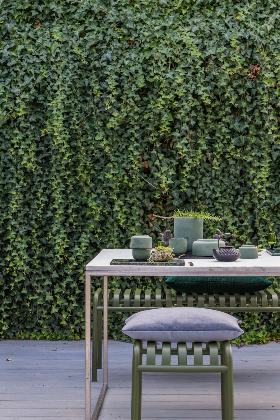 Mesa de terraza con pisos, de color gris. Atrás se de un gran muro cubierto de hiedra verde