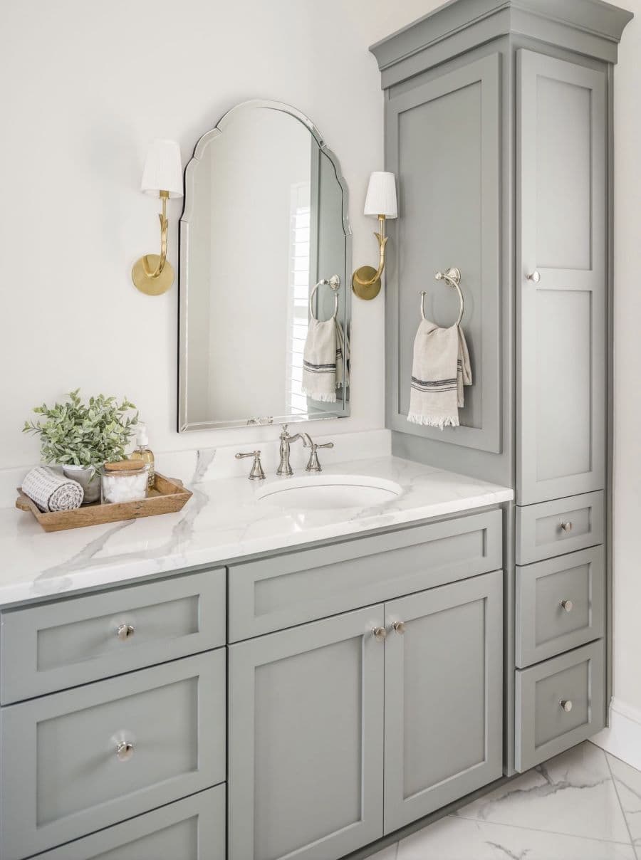 Baño con muebles grises y base de mármol. Espejo estilo vintage con marco plateado y grifería plateada.