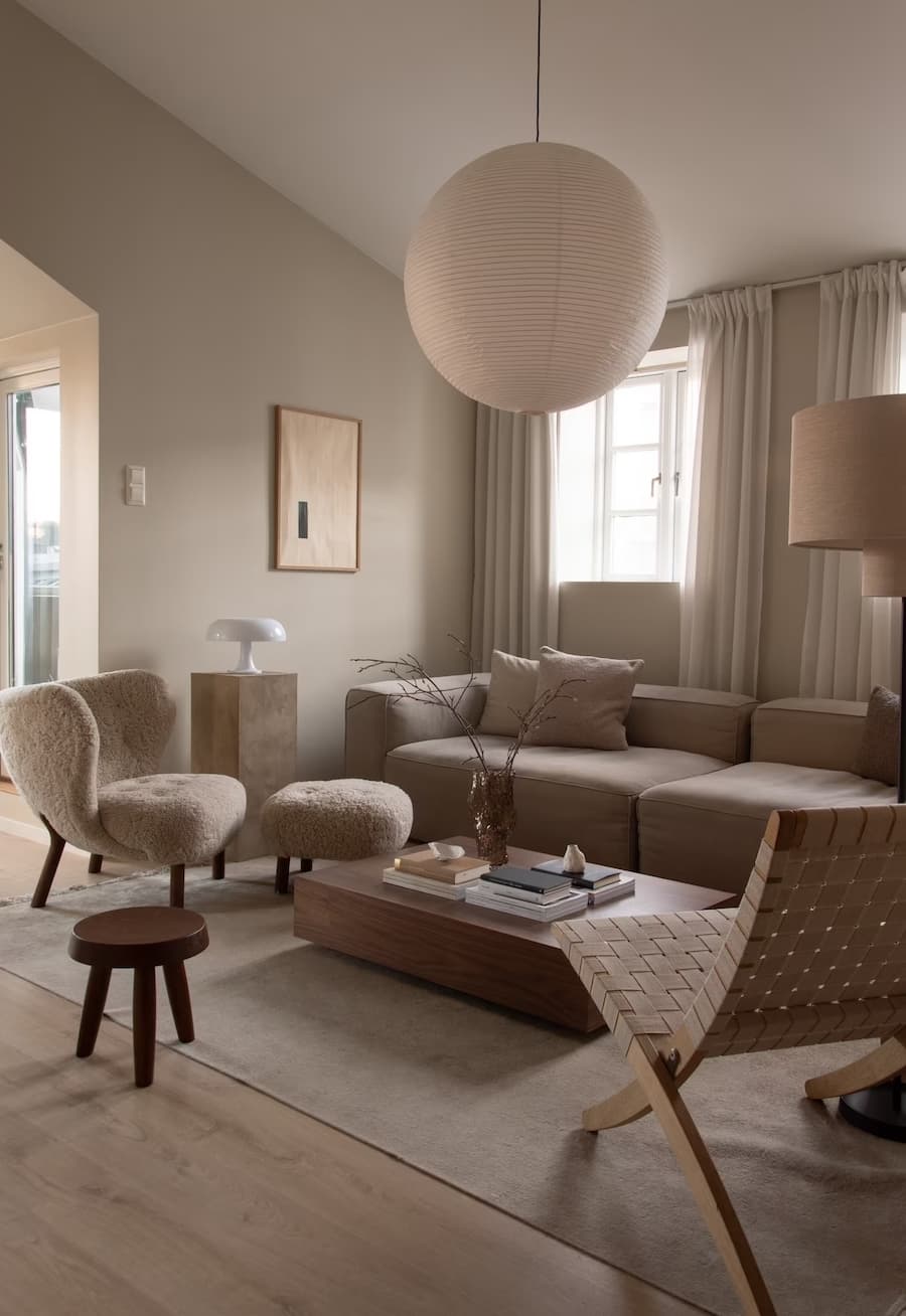 Living de estilo tradicional con sillón y sitial color greige. Mesa de centro de madera y gran lámpara colgante de papel, redonda y blanca