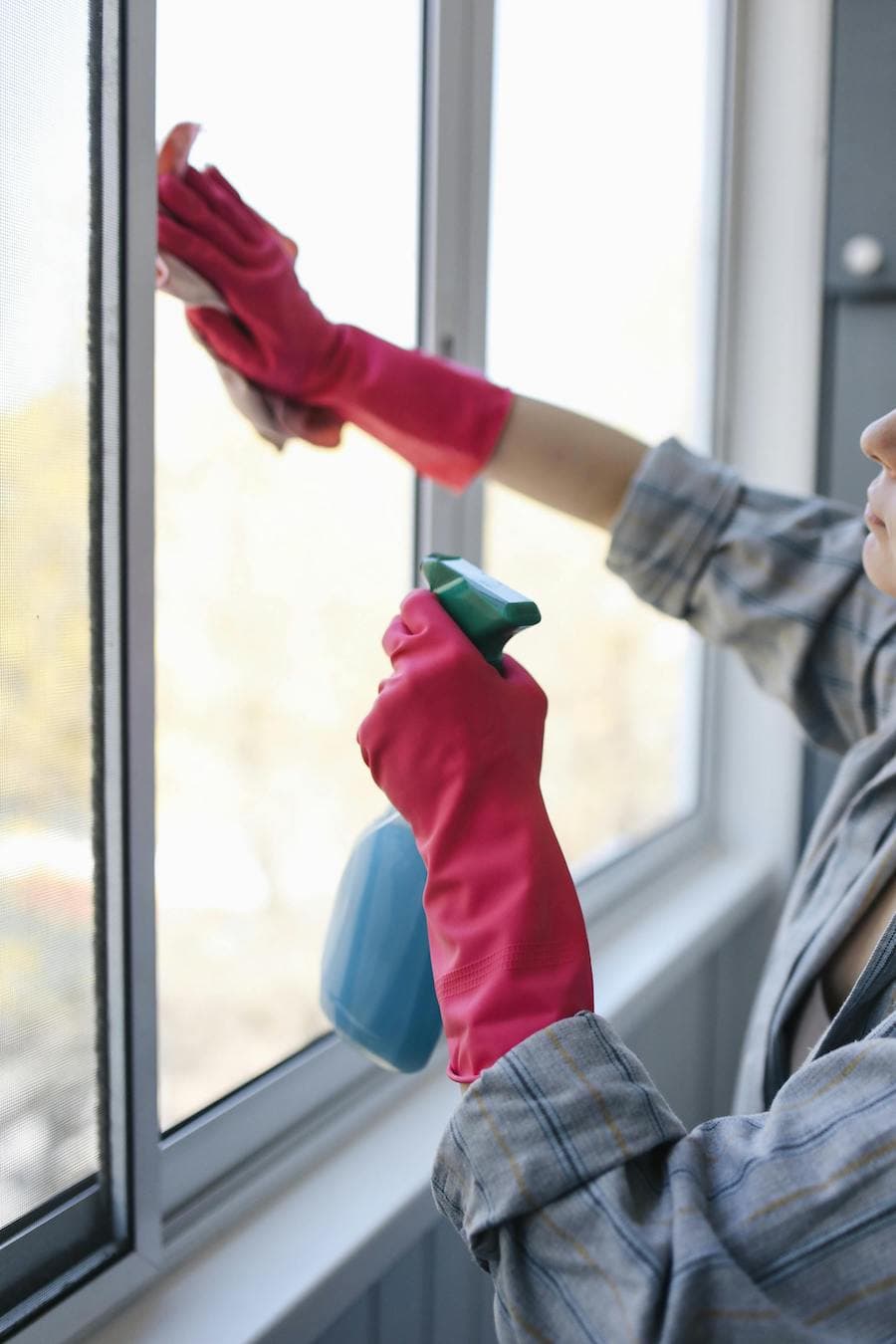 Mujer limpiando una ventana con guantes rosados.