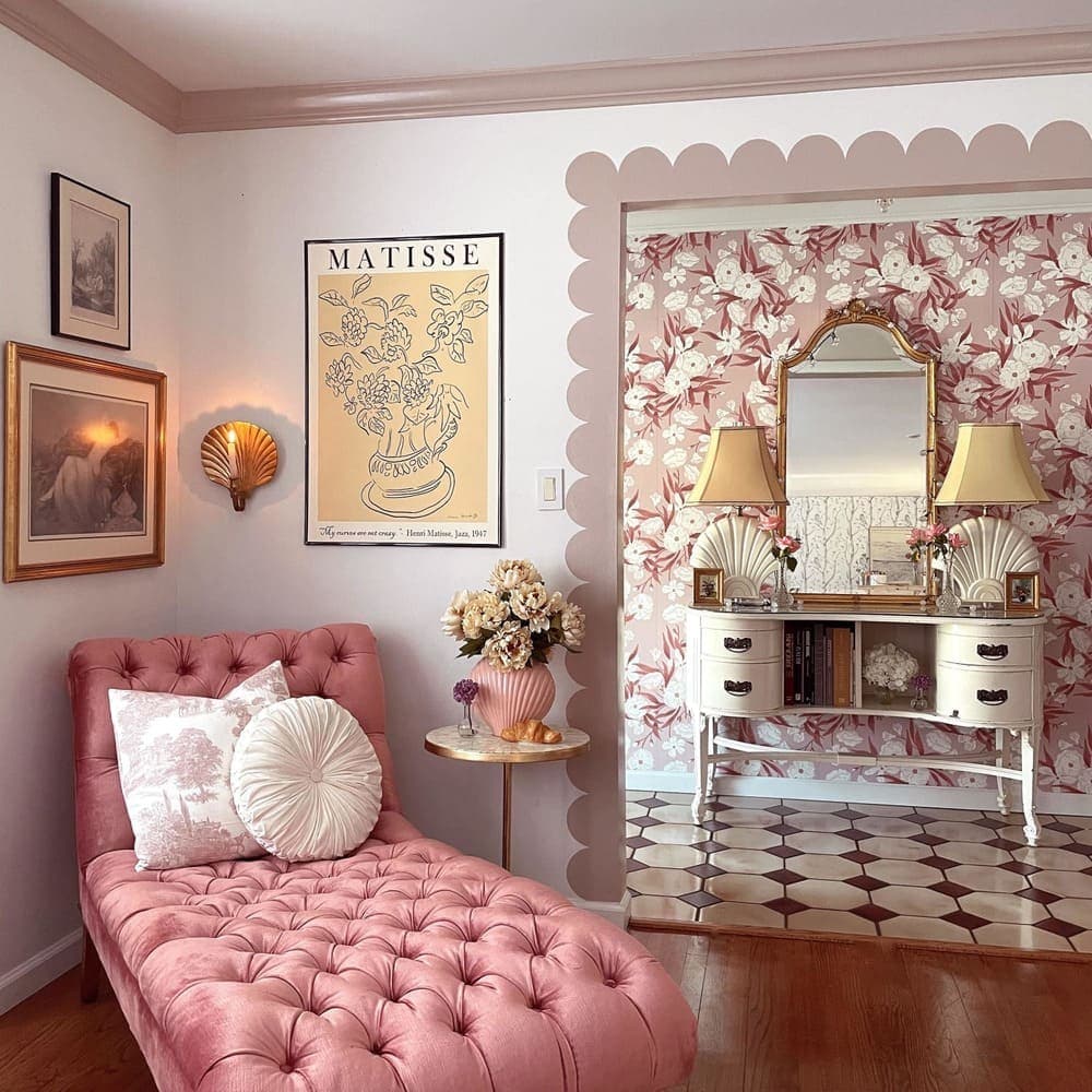 Habitacion estilo coquette con un chaise longue rosa capitoné, al fondo hay un pasillo con un mueble recibidor ewtilo clásico con un gran espejo y dos lámparas.