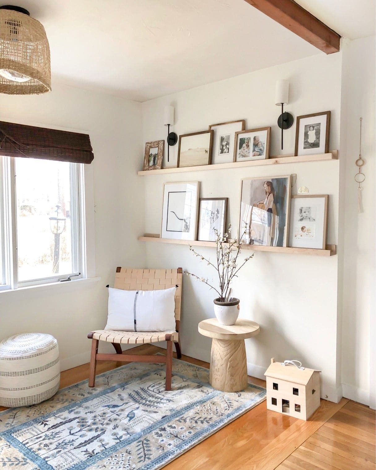 Espacio del hogar con dos repisas de madera que sostienen marcos con fotos e ilustraciones. En la misma pared hay dos apliqués negros con pantalla blanca. Debajo de las repisas hay una poltrona y una mesa lateral de madera, que están sobre una alfombra.