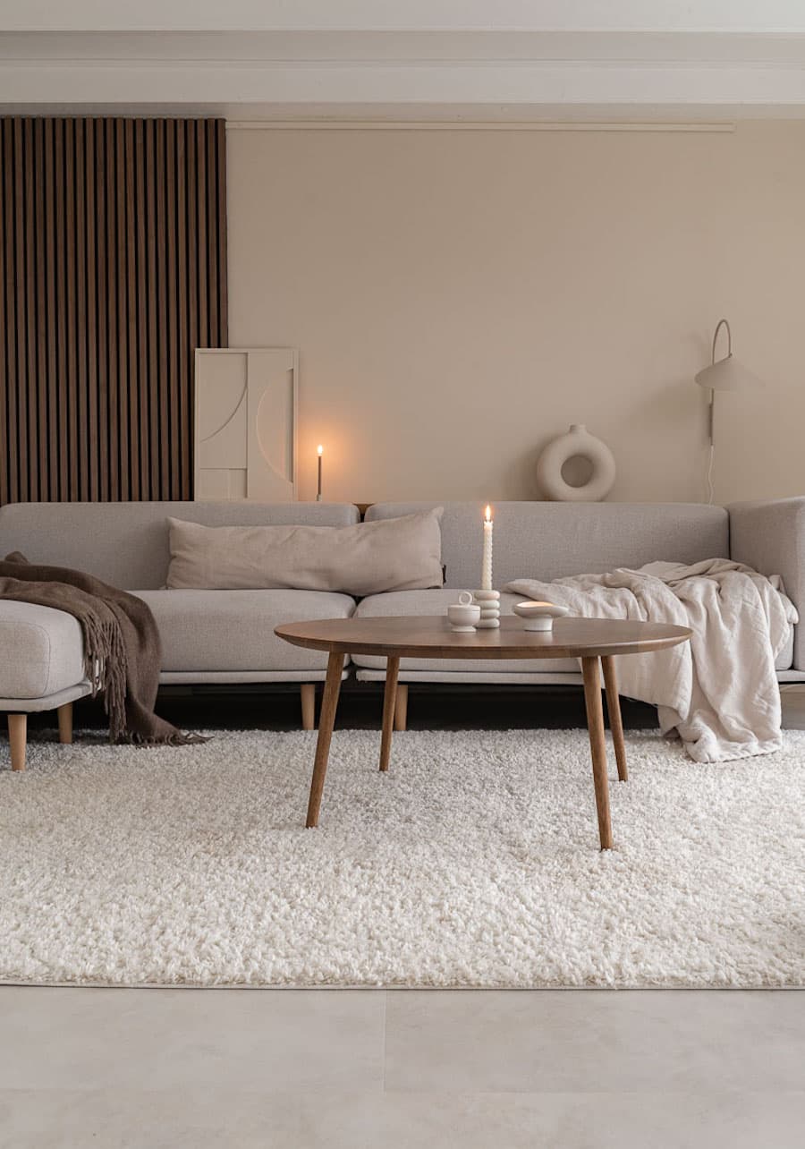 Living cálidos con muros color greige, Gran sofá en L gris claro, mesa de centro de madera y textiles beige y café. 