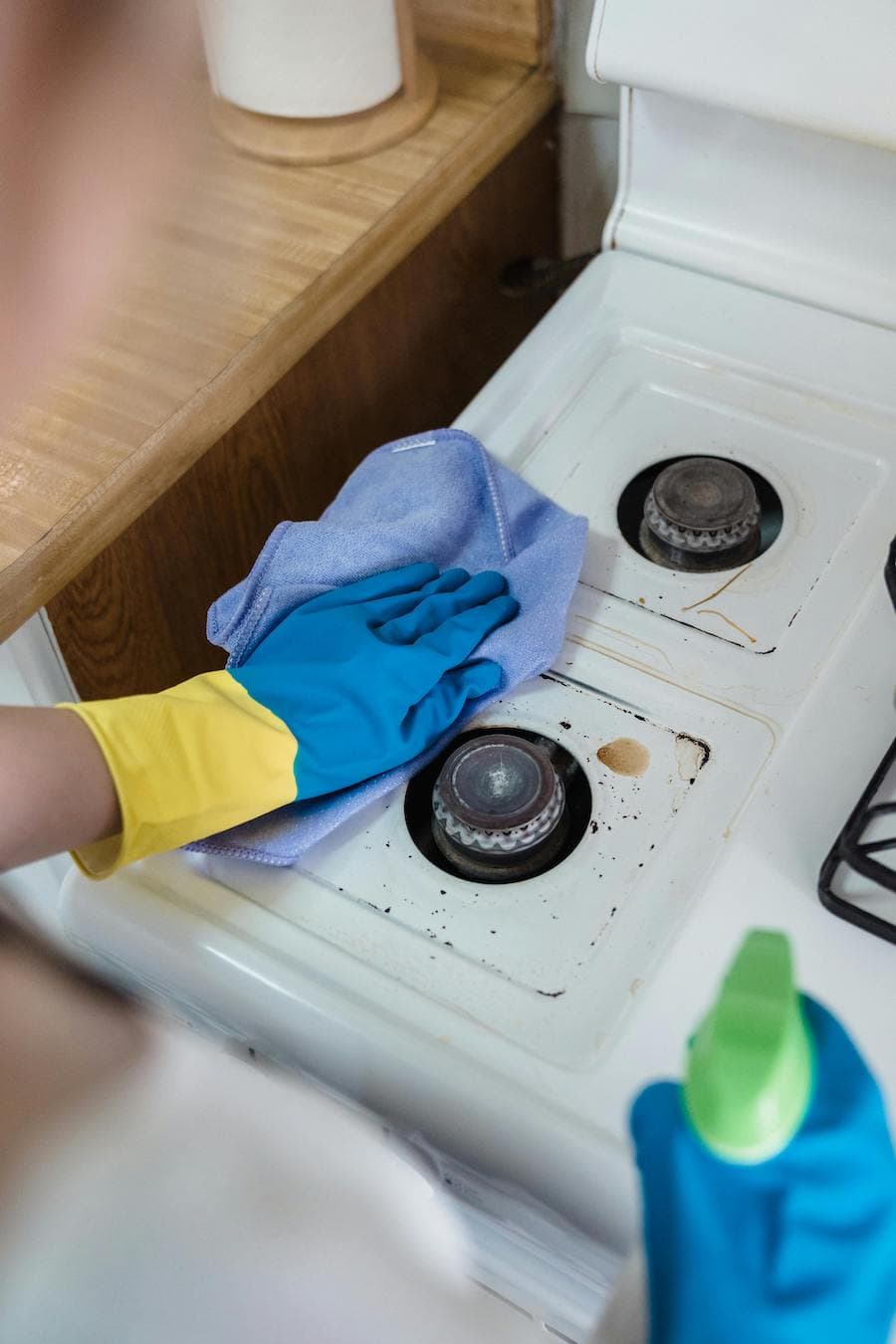 Tips de limpieza, manos con guantes azules limpiando con un paño celeste los fuegos de una cocina blanca.