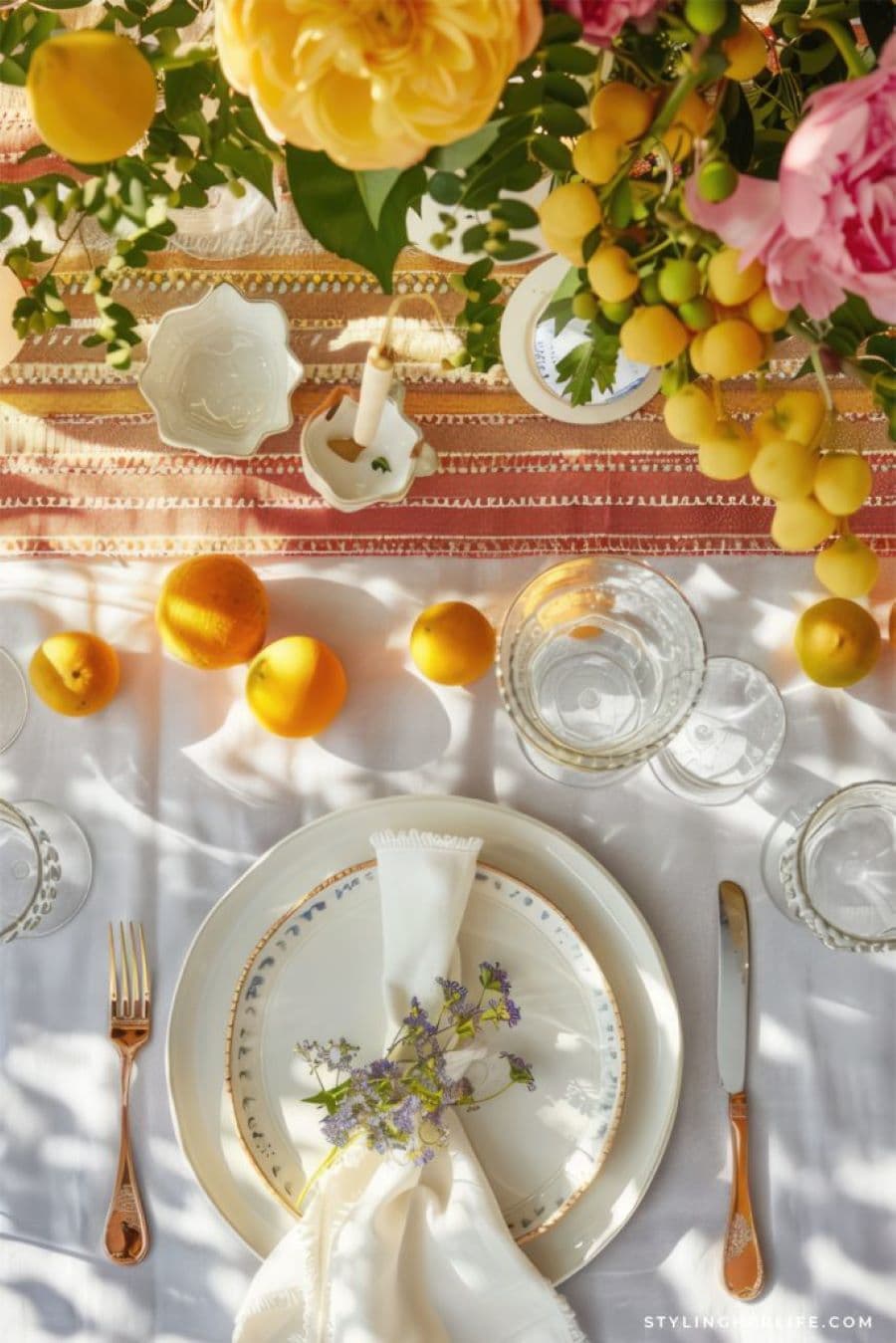 Mesa de verano con vajilla combinada. Mantel blanco con copas y vasos de vidrio. La vajilla es combinada, con plato grande liso y moderno, y plato pequeño con detalles de flores en el borde.