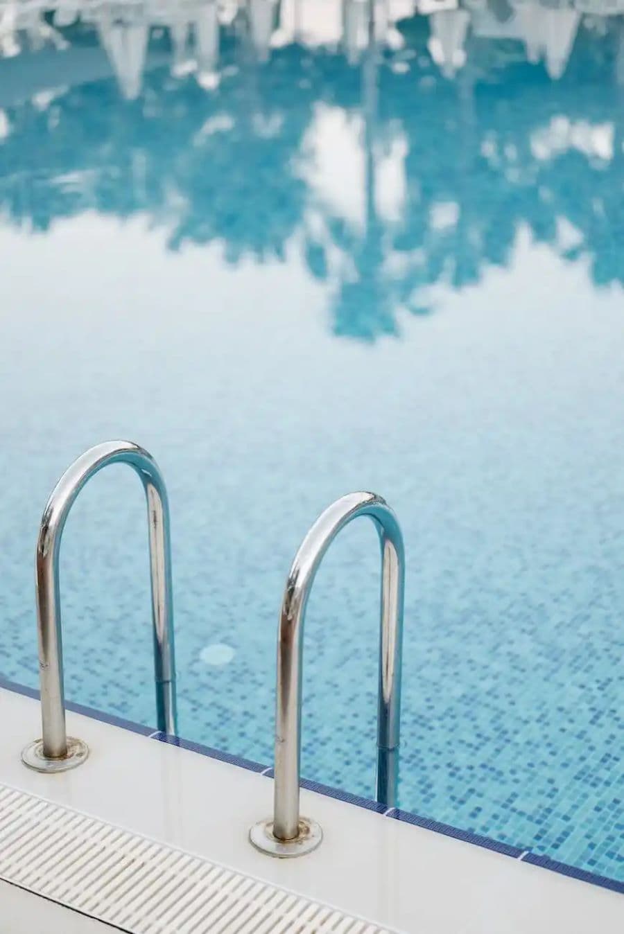 Gran piscina con una escalera con dos barandas metálicas que entran al agua. Borde de concreto color gris claro