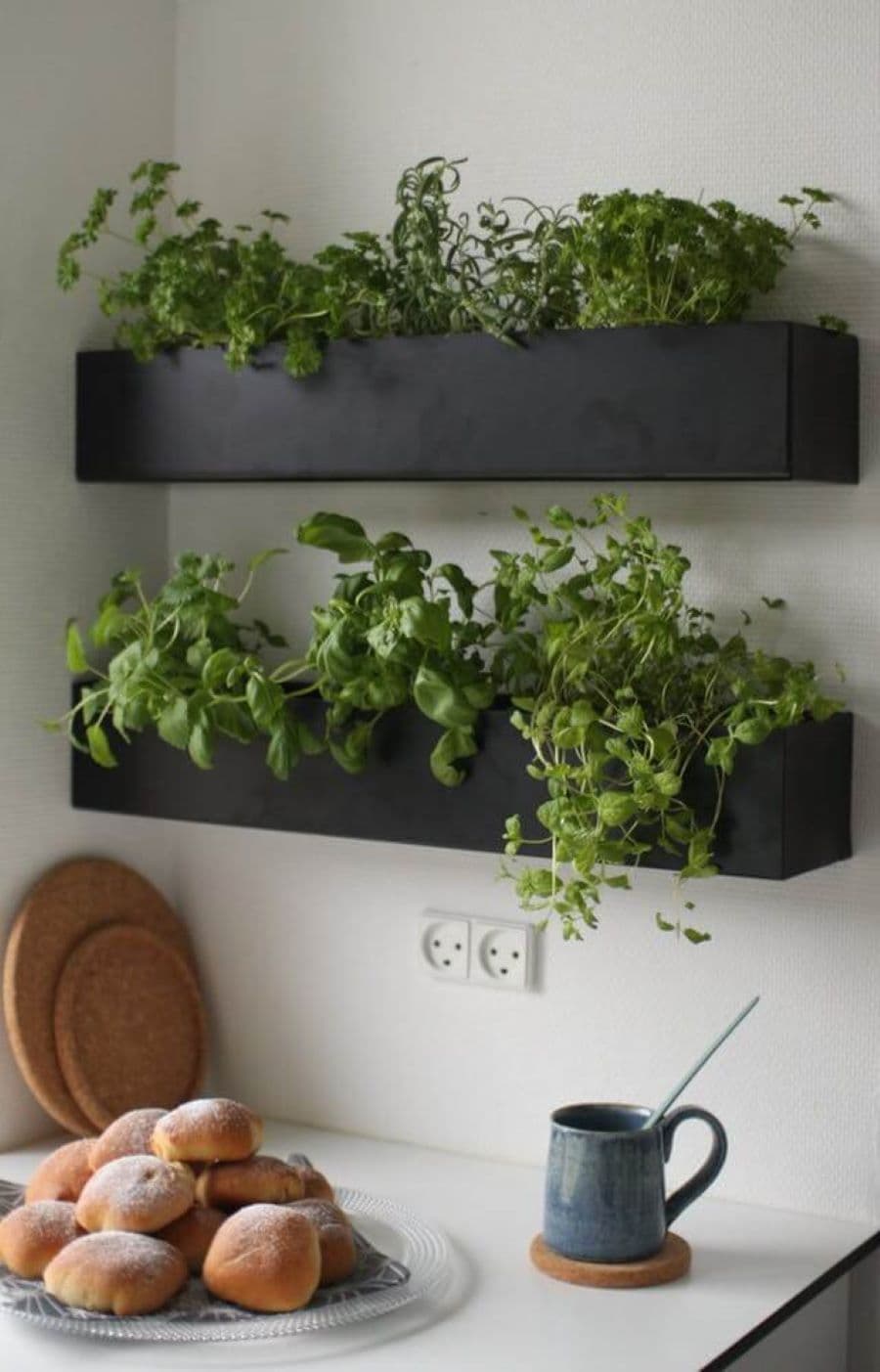 Cocina con mini huerto en dos maceteros negros flotantes. Muro blanco, tablas de cocina de madera.