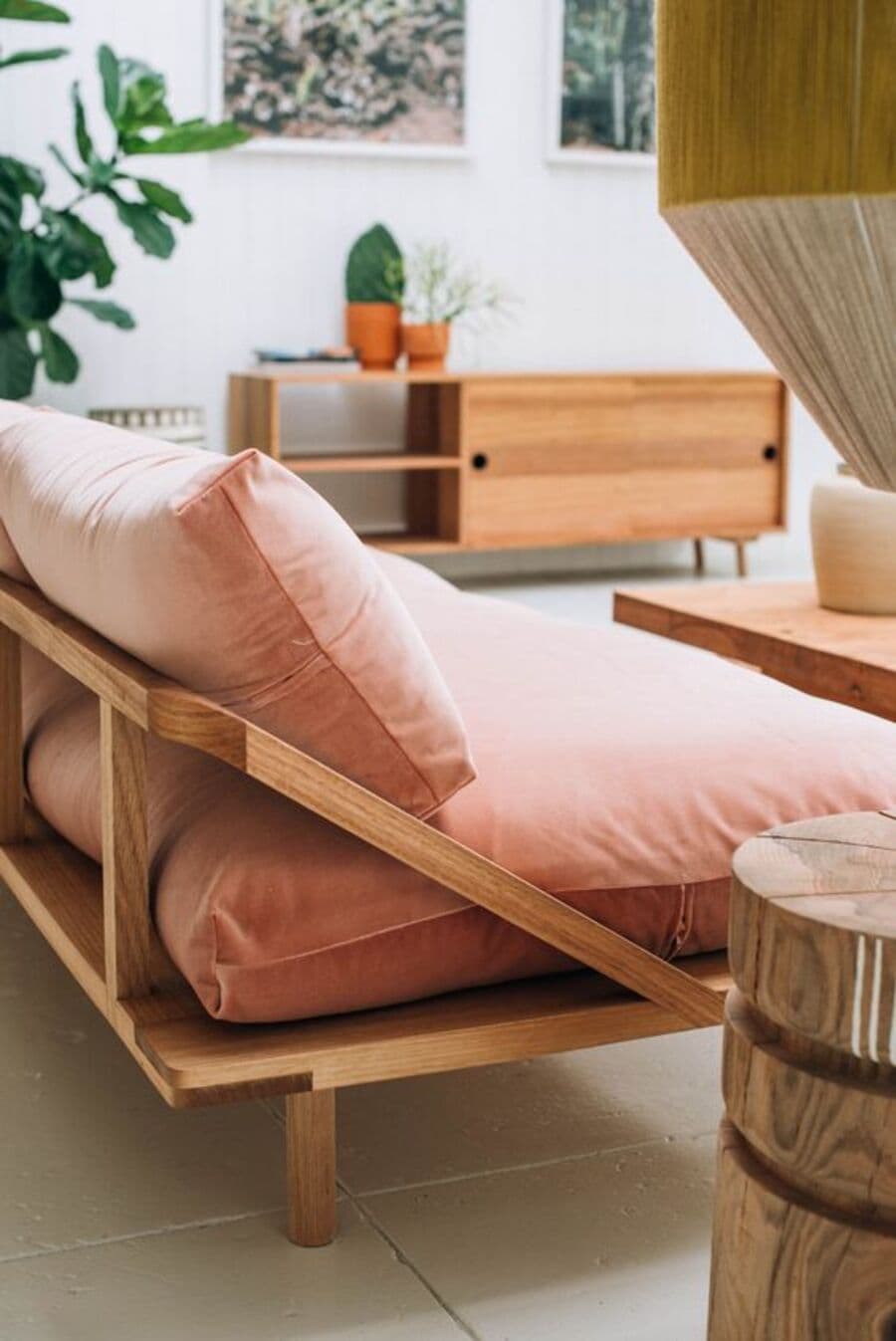 Sillón de base de madera con cojines color Peach fuzz en tela de lino. Atrás se ve un arrimo de madera con una repisa y puerta corredera. Al lado del sillón hay una mesa de apoyo de madera, redonda. Plantas