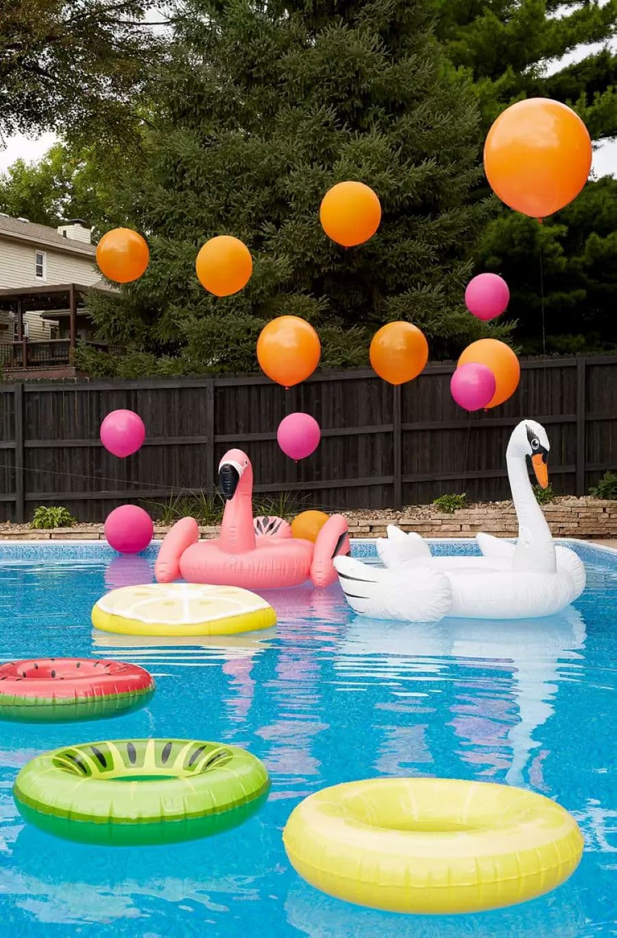 Piscina grande con dos flotadores con forma de cisne y flamenco. Tres flotadores redondos con diseño de limón, sandía y kiwi. Globos con helio rosados y naranjos.