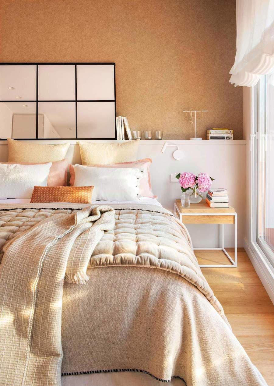 Dormitorio de tonos mostaza con un espejo estilo ventana de marco negro sobre el cabecero de la cama. 