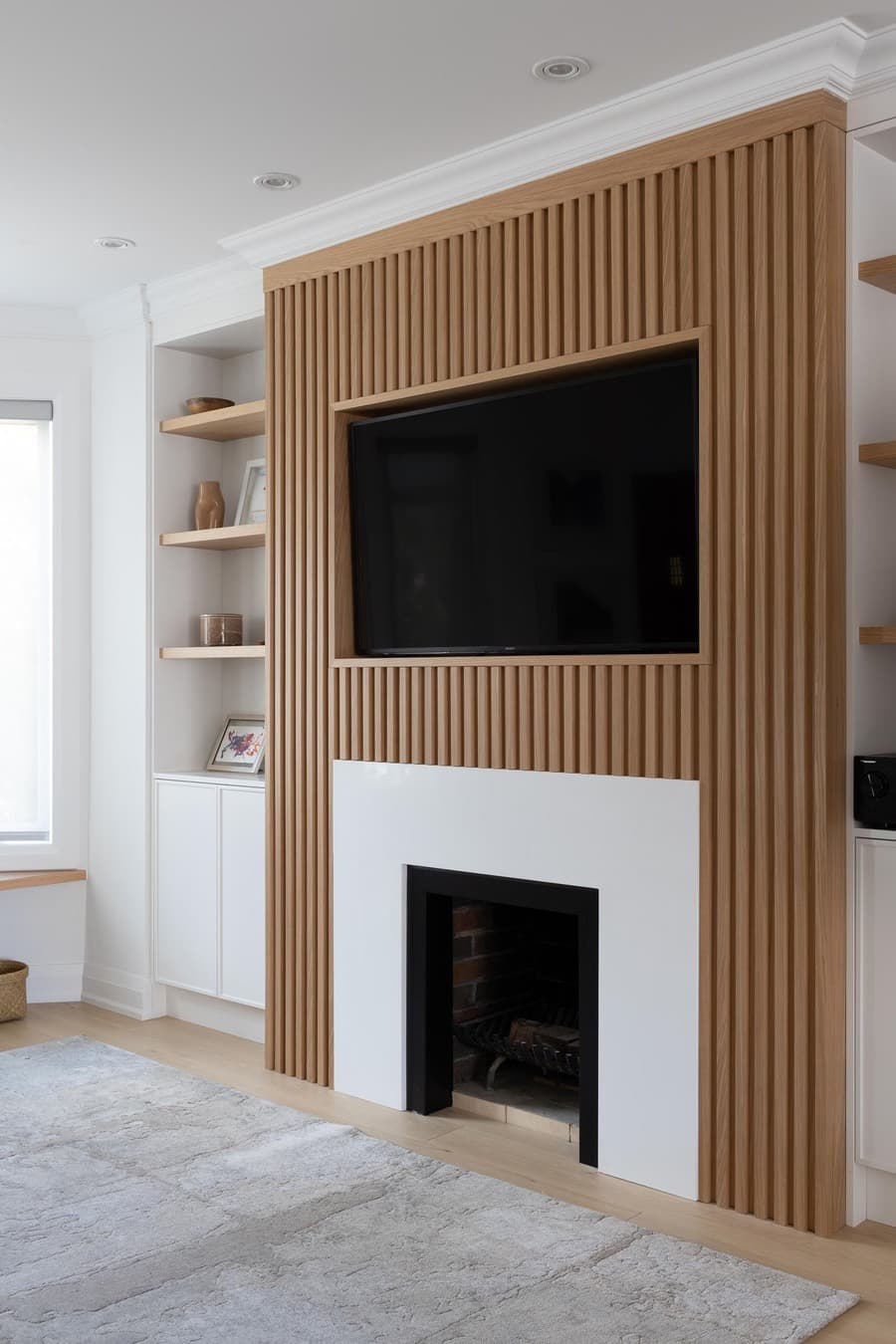 Living con una pared con un revestimiento de madera con un televisor y una chimenea debajo, y estantes de madera a los costados.