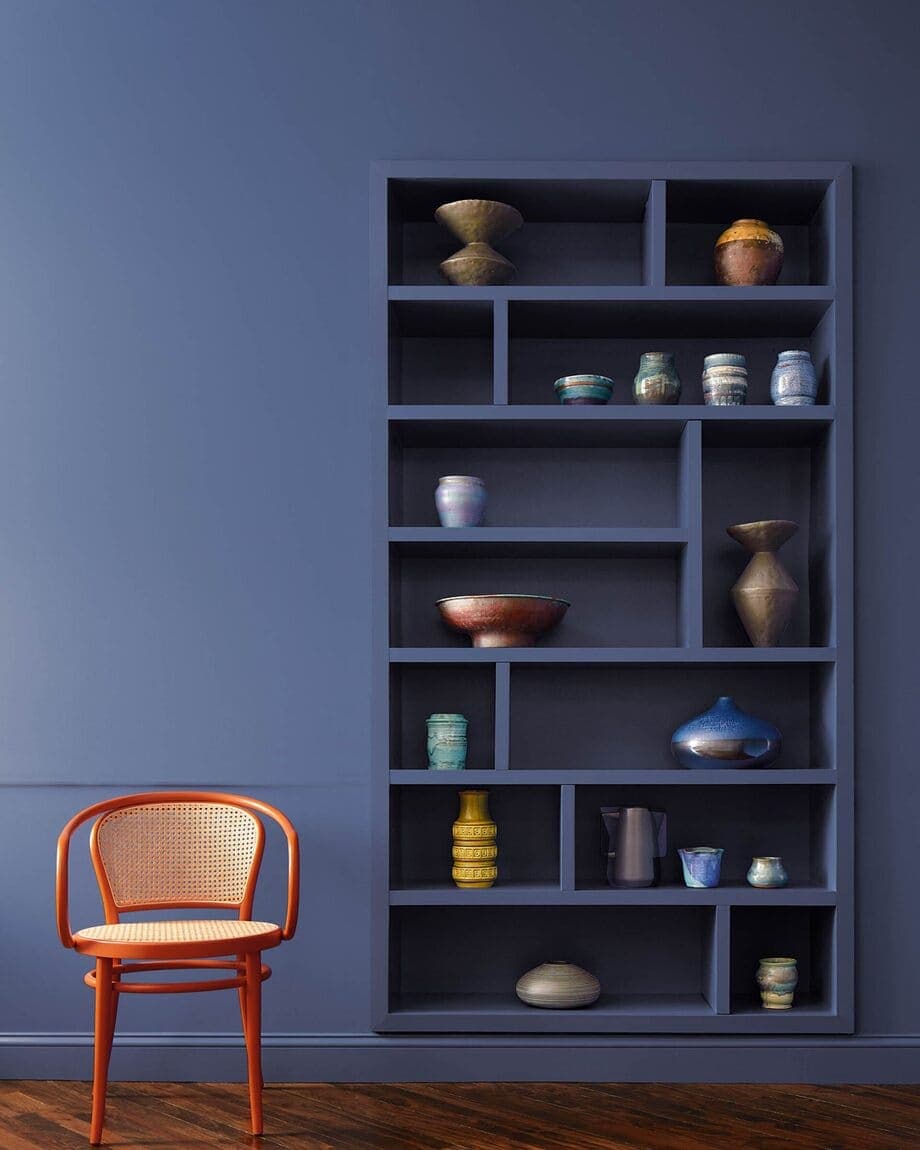 Espacio del hogar con un estante y pared color Blue nova. También hay una silla de mimbre con estructura color rojo.