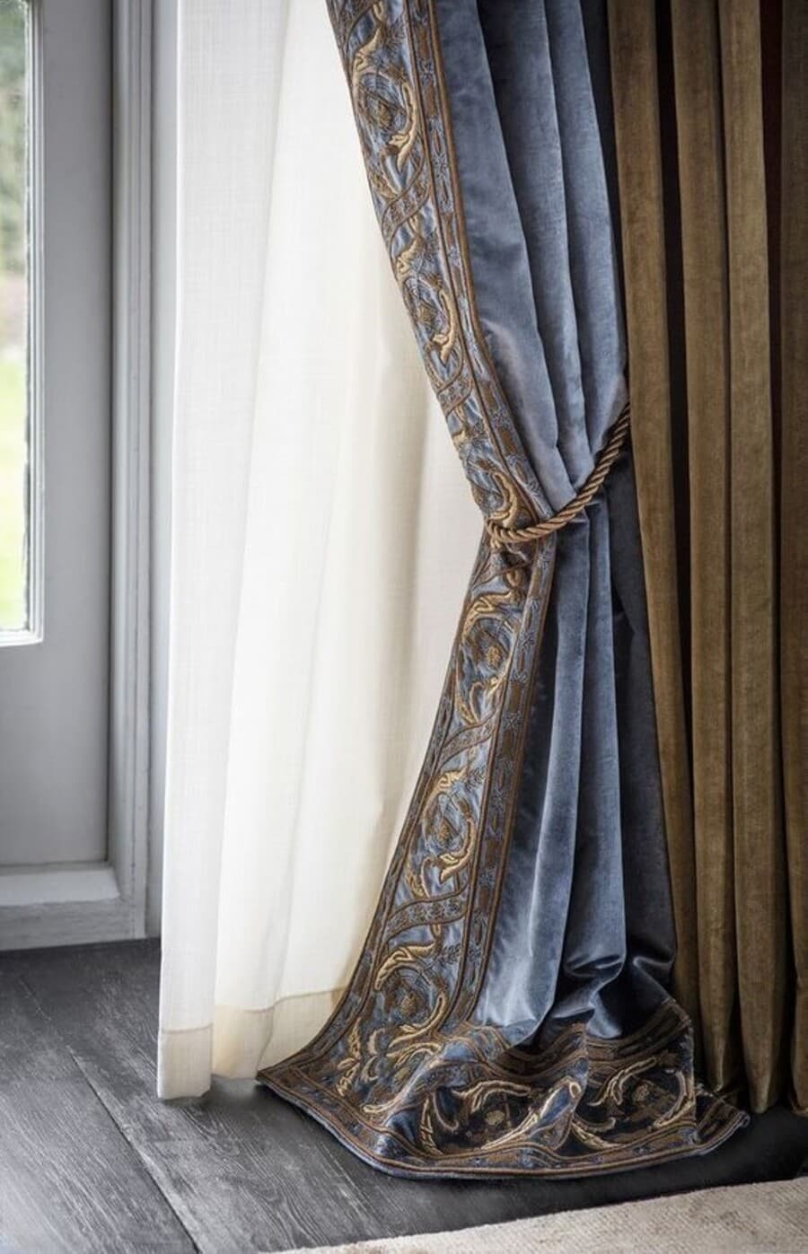 Detalle de cortinas combinadas. Cortina de tela blanca y cortina de terciopelo azul con diseño bordado en los extremos. Amarras de cortina de terciopelo.