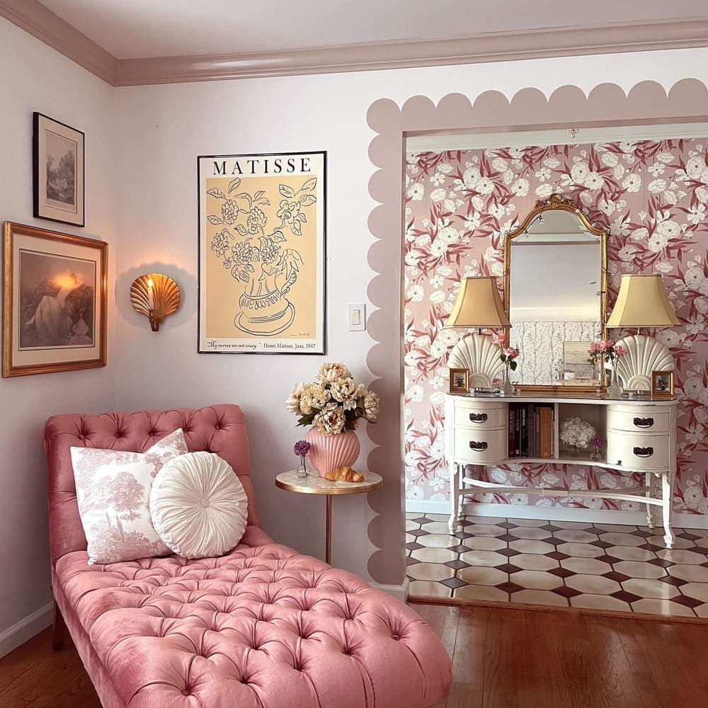 Habitacion estilo coquette con un chaise longue rosa capitoné, al fondo  hay un pasillo con un mueble recibidor ewtilo clásico con un gran espejo y dos lámparas.