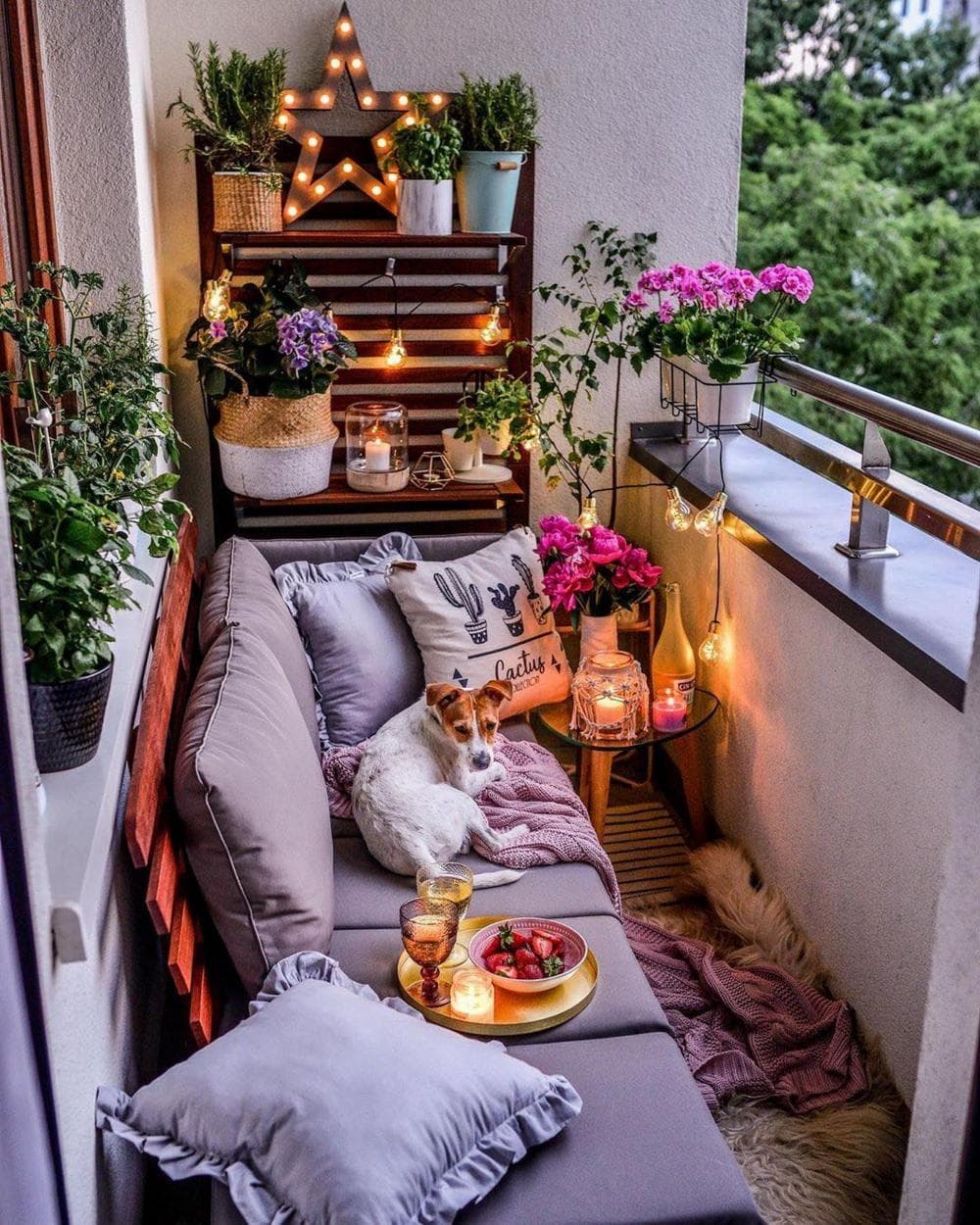 Balcón con un sofá color gris, un pequeño espacio para macetas con flores y guirnaldas.