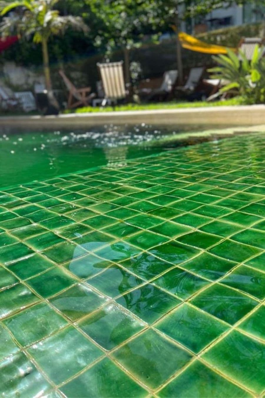 Detalle de piscina con azulejos cuadrados de color verde. El agua de la piscina se ve verde.