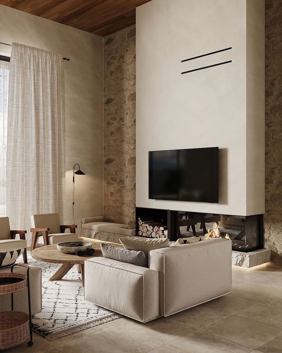 Sala de estar en tonos croma con una chimenea con un televisor sobre ella, y muros de piedra en el muro detrás de la chimenea. Hay un sofá beige, una mesa de centro redonda de madera clara sobre una alfombra blanca con líneas grises.