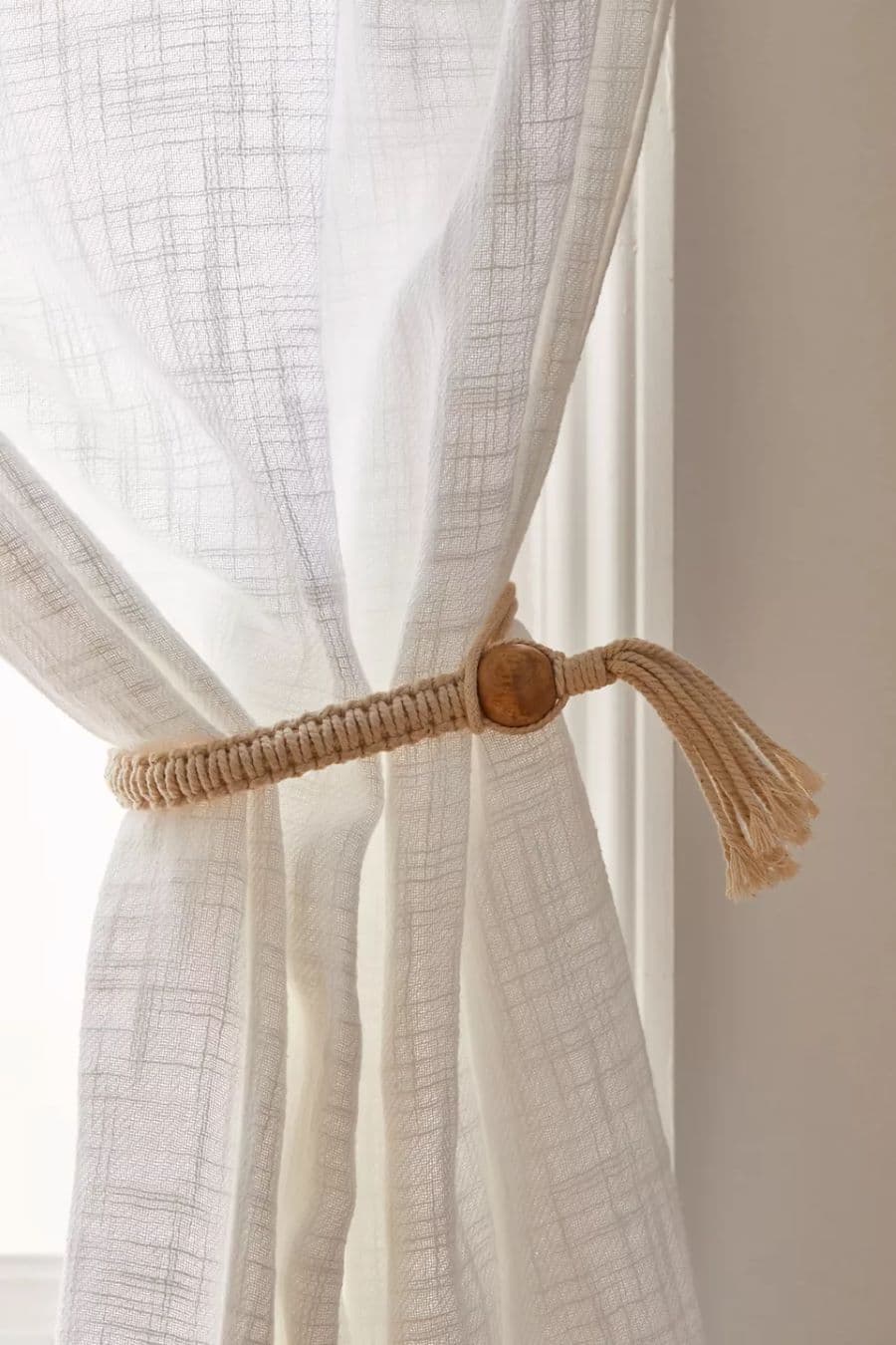 Detalle de cortina visillo. Tela delgada blanca con una amarra de cordel de algodón tejida y una borla de madera.