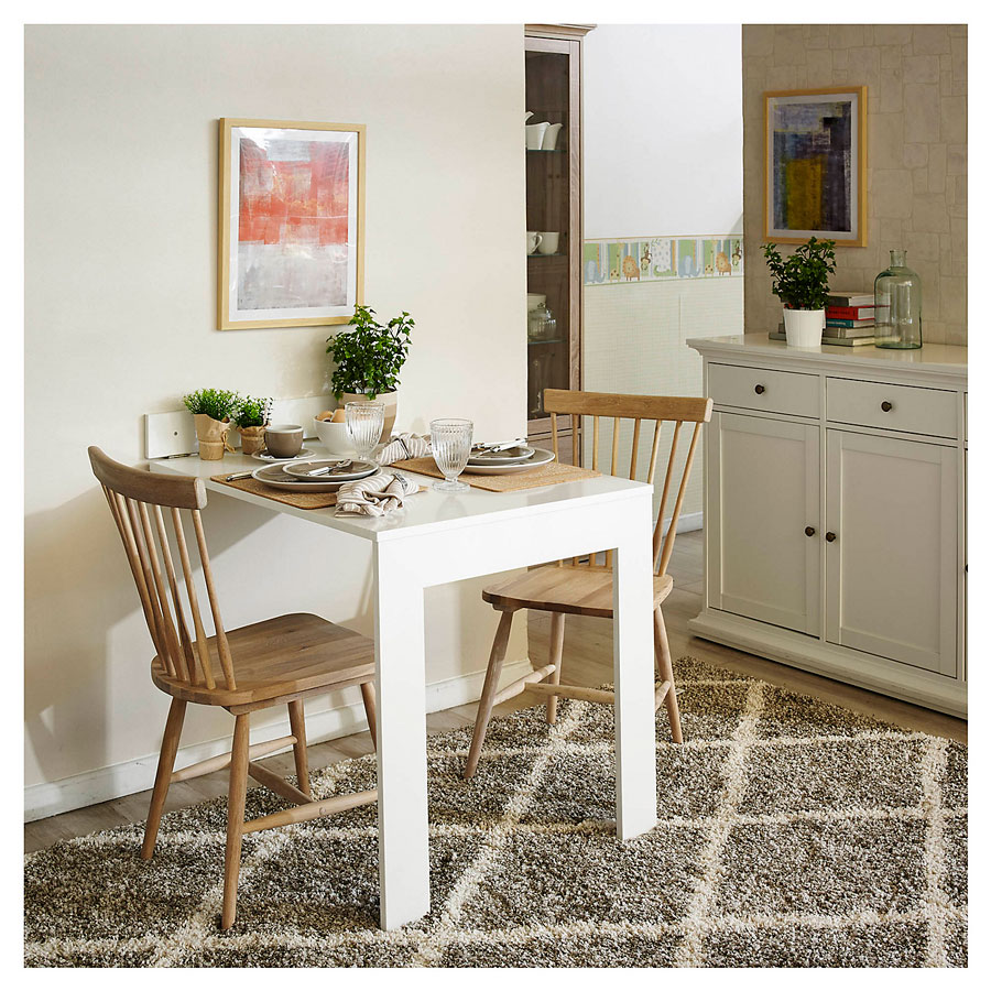 Comedor pequeño con una mesa blanca empotrada a la pared y dos sillas de madera. Están sobre una alfombra shaggy gris con patrones de rombos color crema. Al fondo hay un buffet blanco.