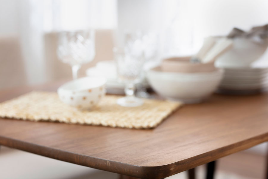 close up de una mesa e madera con individual tejido con bowls, copas y platos encima.
