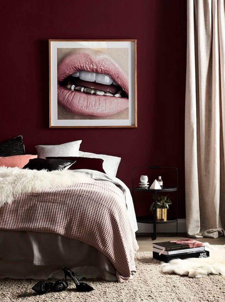 Dormitorio con decoración en tonos rojizos, muros bureo y con una fotografía enmarcada de una boca pintada de rosa
