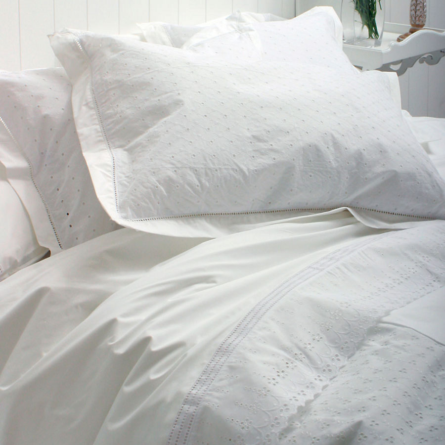detalle de cama con juego de sábanas blanca, dos almohadones blancos.