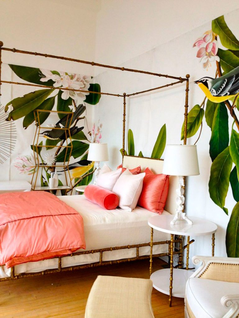 Dormitorio veraniego, decorado con cojines y mantas en coral, muros blancos y murales de hojas tropicales y pájaros.