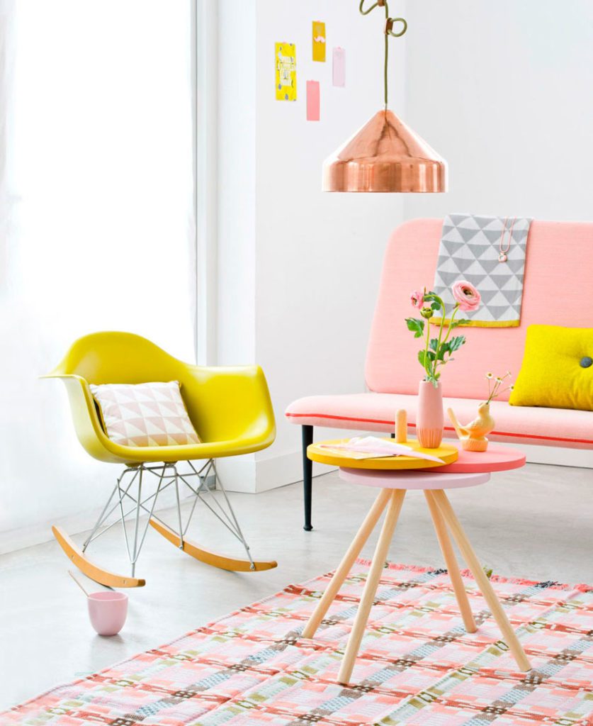living con una silla mecedora en amarillo, lámpara colgante de cobre, sillón en color durazno y una mesa de centro de madera en diferentes colores rosa, amarillo y durazno