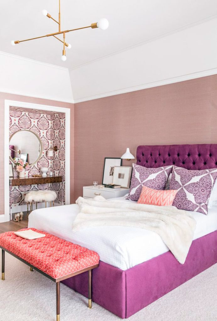 Dormitorio moderno, con una cama en tonos lila y blanco, y una banqueta coral.
