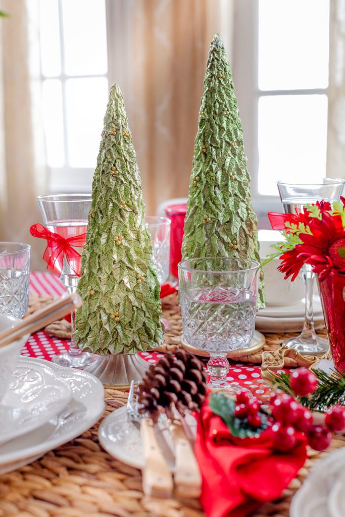Dos pinos de navidad de resina verdes, como decoración de mesa, junto a copas de cristal