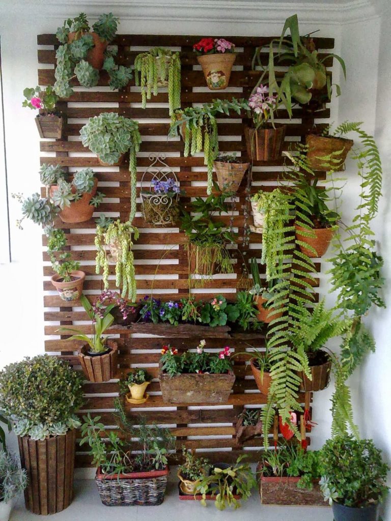 Jardinera de madera con diferentes maceteros, plantas y enredaderas verdes, así como flores.