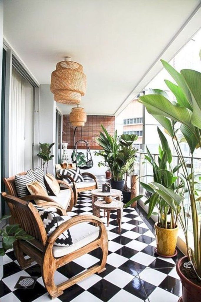 Balcón en blanco y megro con muebles y accesorios de madera y mimbre, así como plantas de hojas verdes y grandes.