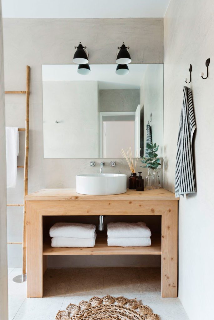Mueble de lavamanos de madera en un baño de muros en color neutro y accesorios de madera