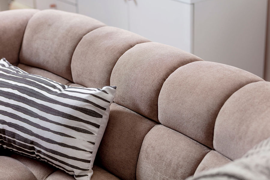 Detalle de un sofá de tercopélo café, junto a un cojín decorativo rayado