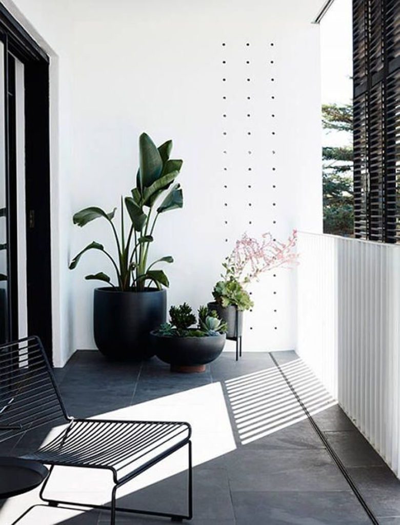 Balcón de estilo minimalista, con paredes blancas, una silla de fierro y solo tres maceteros con plantas verdes