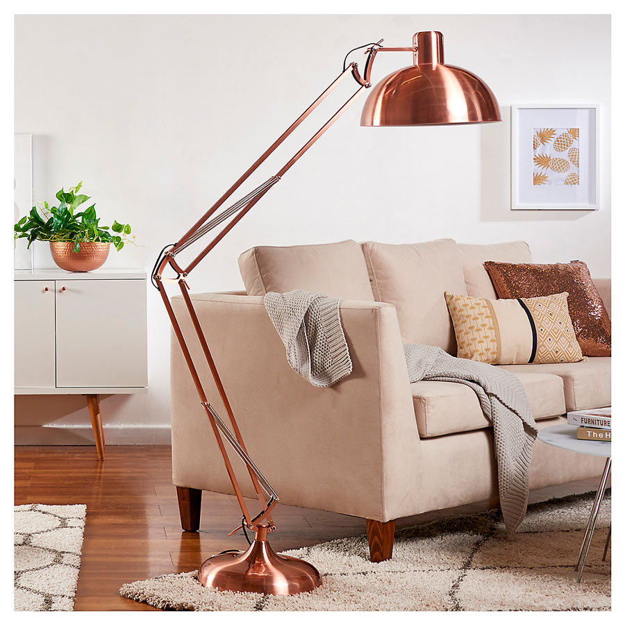 Lámpara flexible de pie, color cobre, en un living con un sofá color café y una alfombra en color crudo.