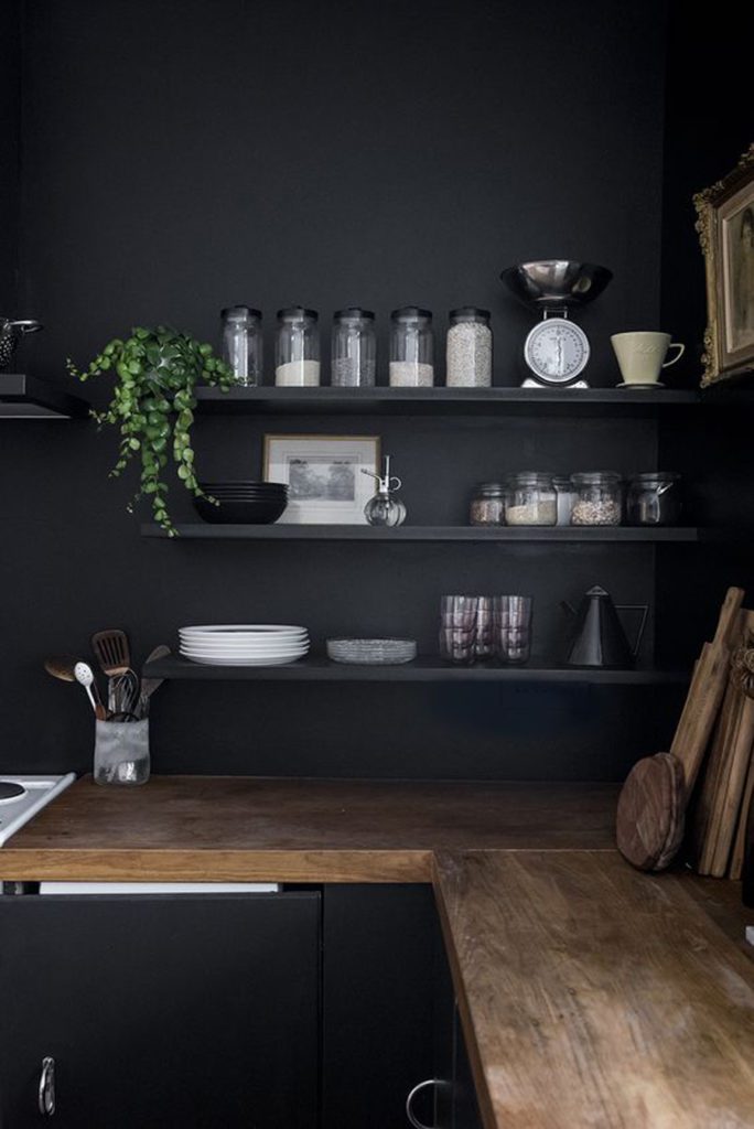 Detalle de cocina en negro, con repisas y muebles negros. Accesorios de madera y vidrio.