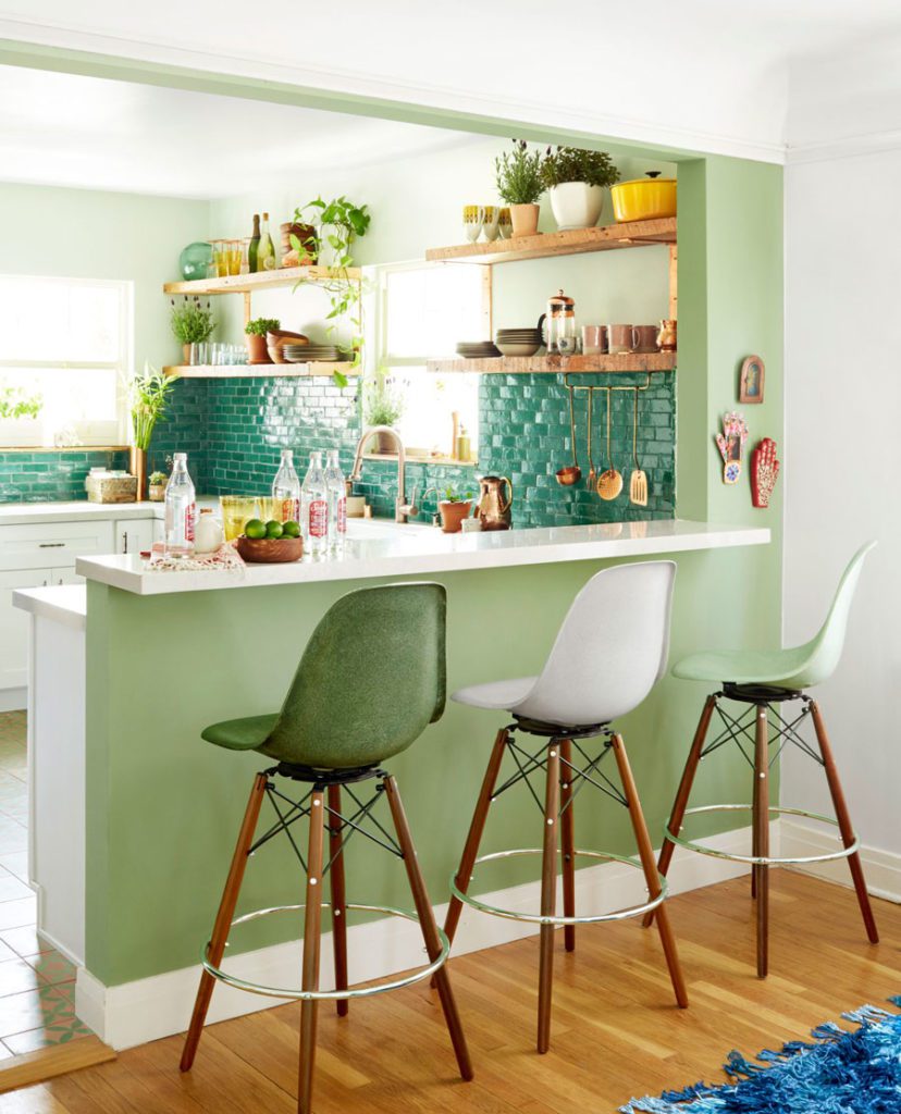 Cocina decorada en tonos verdes, con mesón y tres sillas de bar del mismo modelo en blanco, verde y menta.
