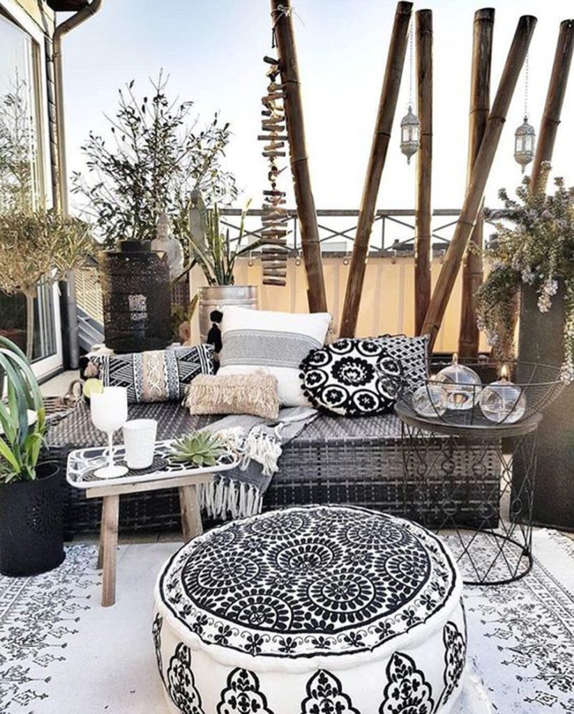 Terraza boho con cojines decorativos con motivos de mandalas en blanco y negro, accesorios de madera y ratán y maceteros con plantas verdes.
