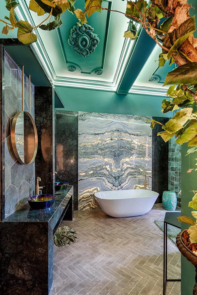Vida de baño en tonos verdes y dorados, con mármol en paredes y muebles, decorado con hojas verdes