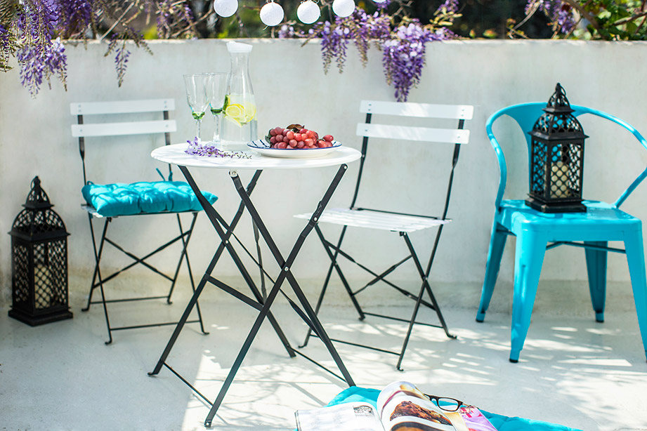 Pequeña mesa de terraza con 2 sillas de color blanco con estructura metálica negra.