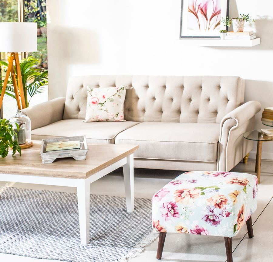 Living con mesa de centro y futón blanco con capitoné, cojines floreados