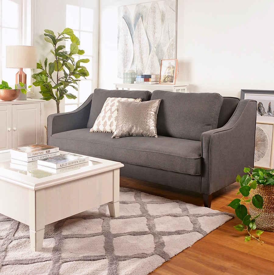 Living con futón color gris, con cojines blanco con gris y uno plateado. Mesa de centro blanca.