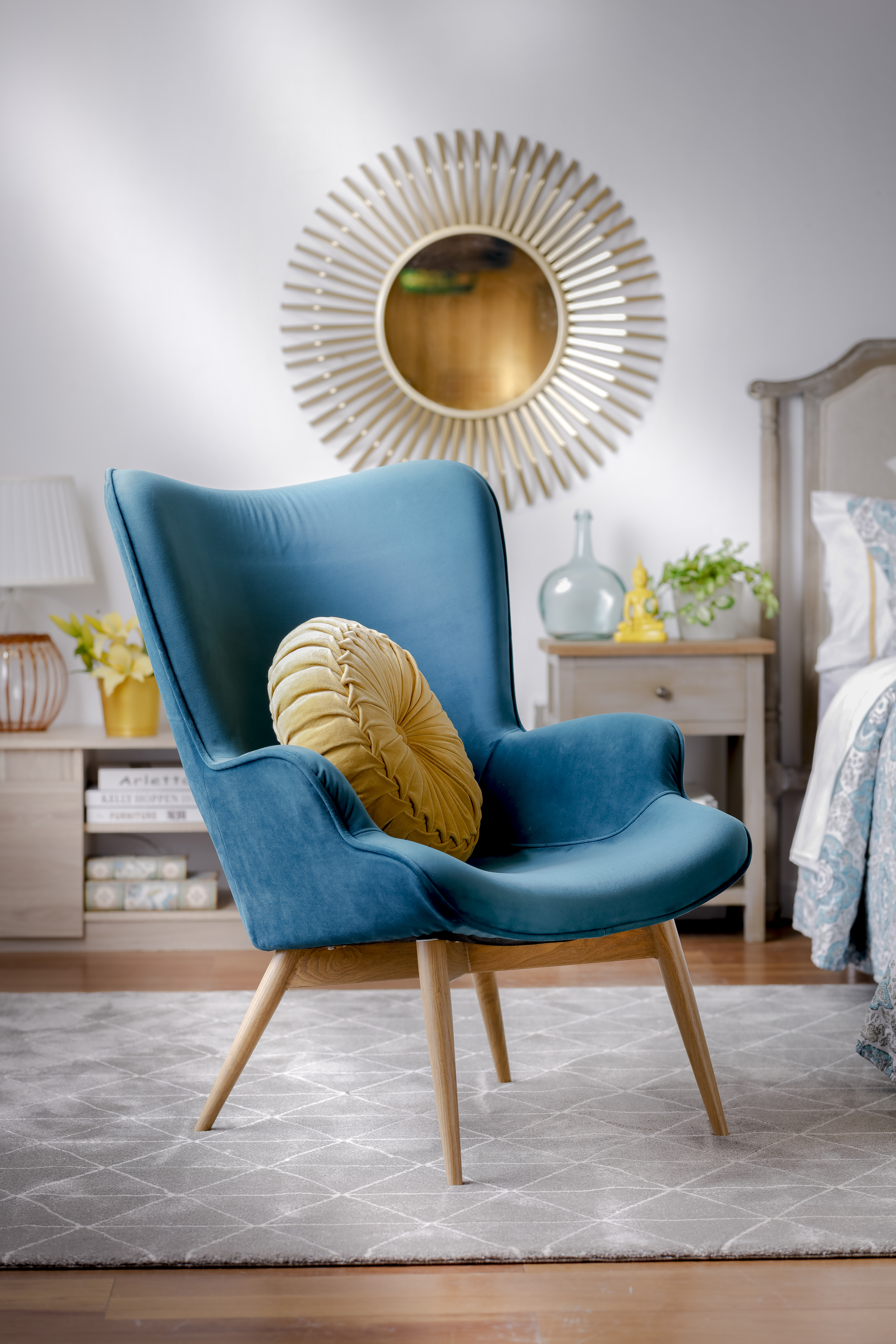 Tendencias de decoración: Ambiente de sala de estar con poltrona terciopelo color calipso y cojín redondo en tono mostaza. De fondo un espejo dorado.