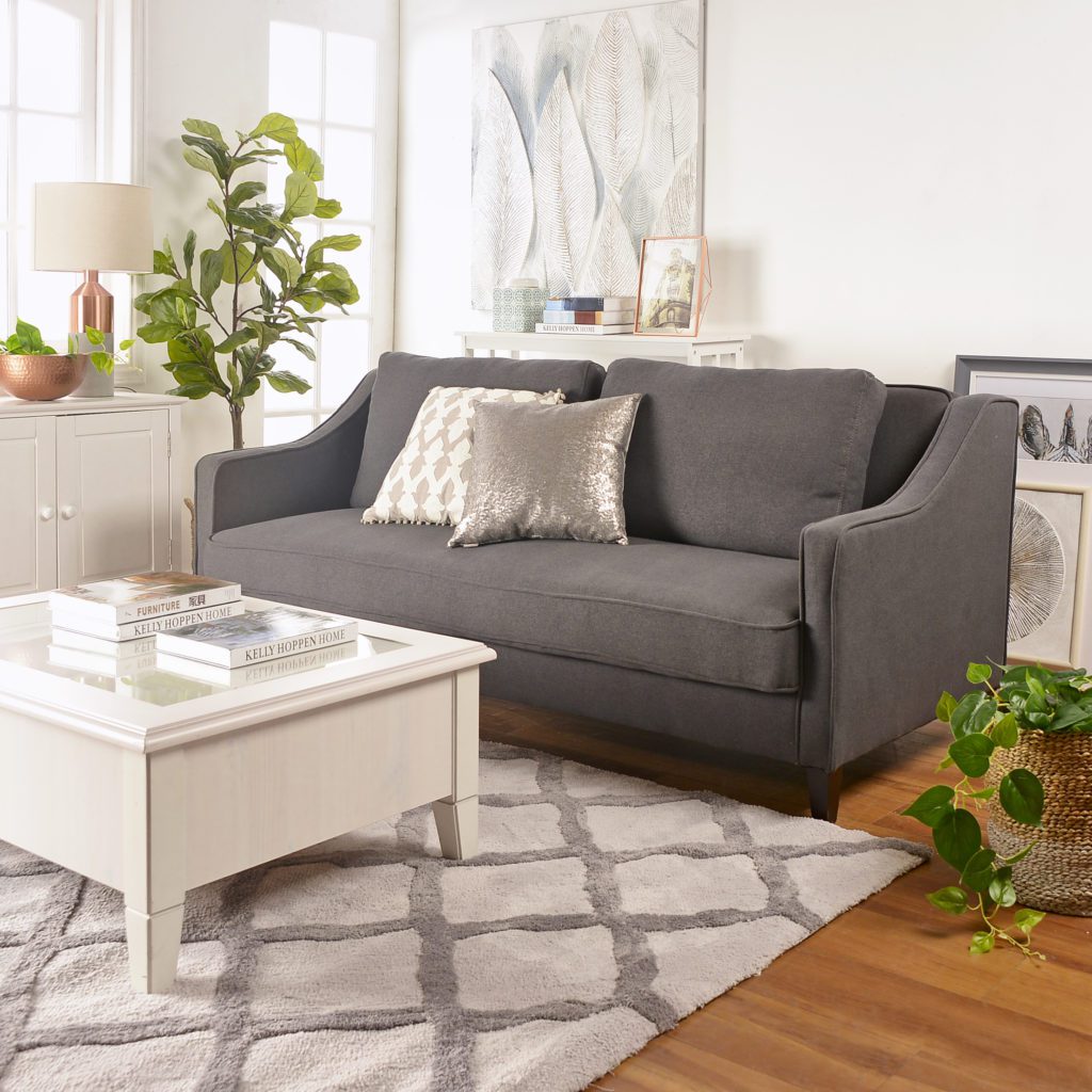Tendencias de decoración: Ambiente de living con un futón color gris, plantas decorativas de hojas verder, mesa blanca de madera y alfombra en los mismo tonos.