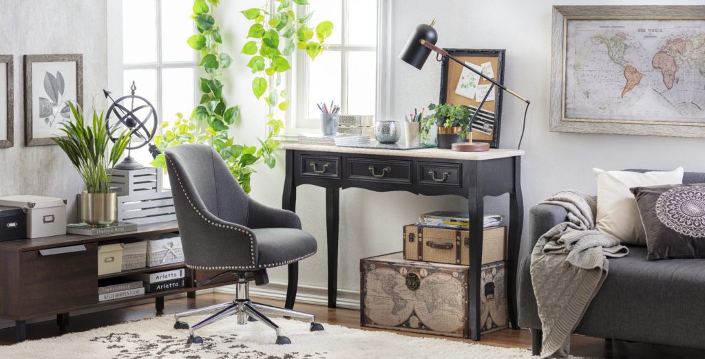Tendencias de decoración: Ambiente sala de trabajo con un escritorio negro clásico con tres cajones pequeños y una silla de cuero. Adornos que invitan a remorar el pasado con mapas, baúles y un futón color gris.