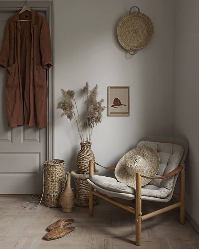 Rincón de un dormitorio con un sitial de mimbre y cojín en tono gris claro, acompañado de canastos en paredes y suelo del mismo material. 