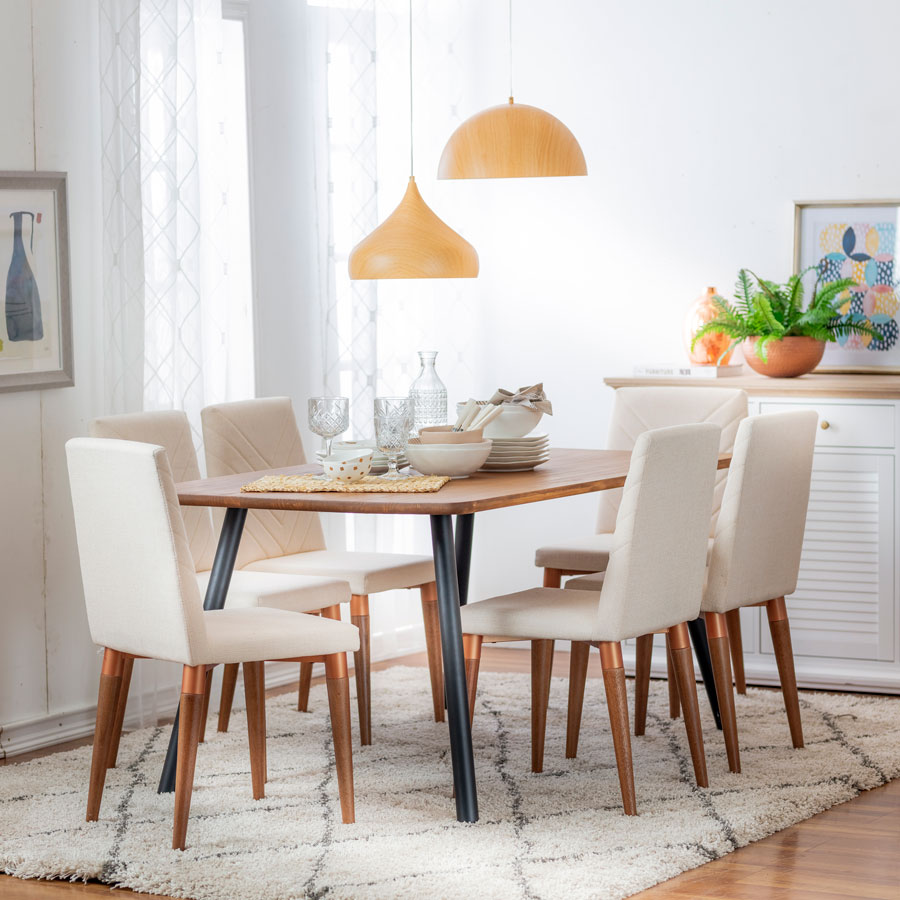 Ambiente de comedor con mesa de madera y patas de meta más 4 sillas en tela color beige y patas de madera. Adornos y alfombra en los mismos tonos.
