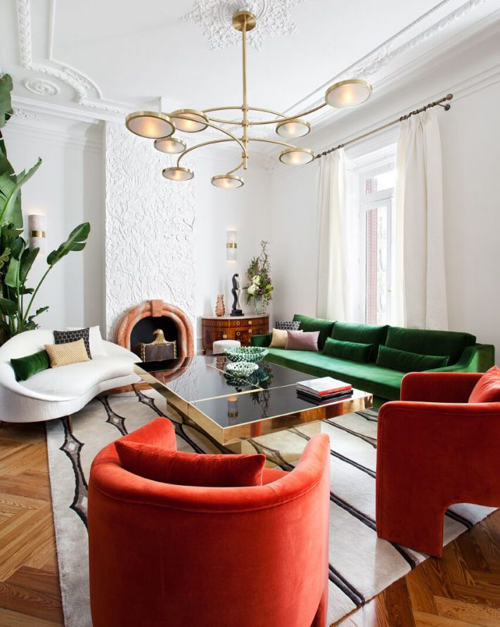 Living estilo maximal minimalism donde destaca un sofá verde botella y dos poltronas rojas con líneas curvas.